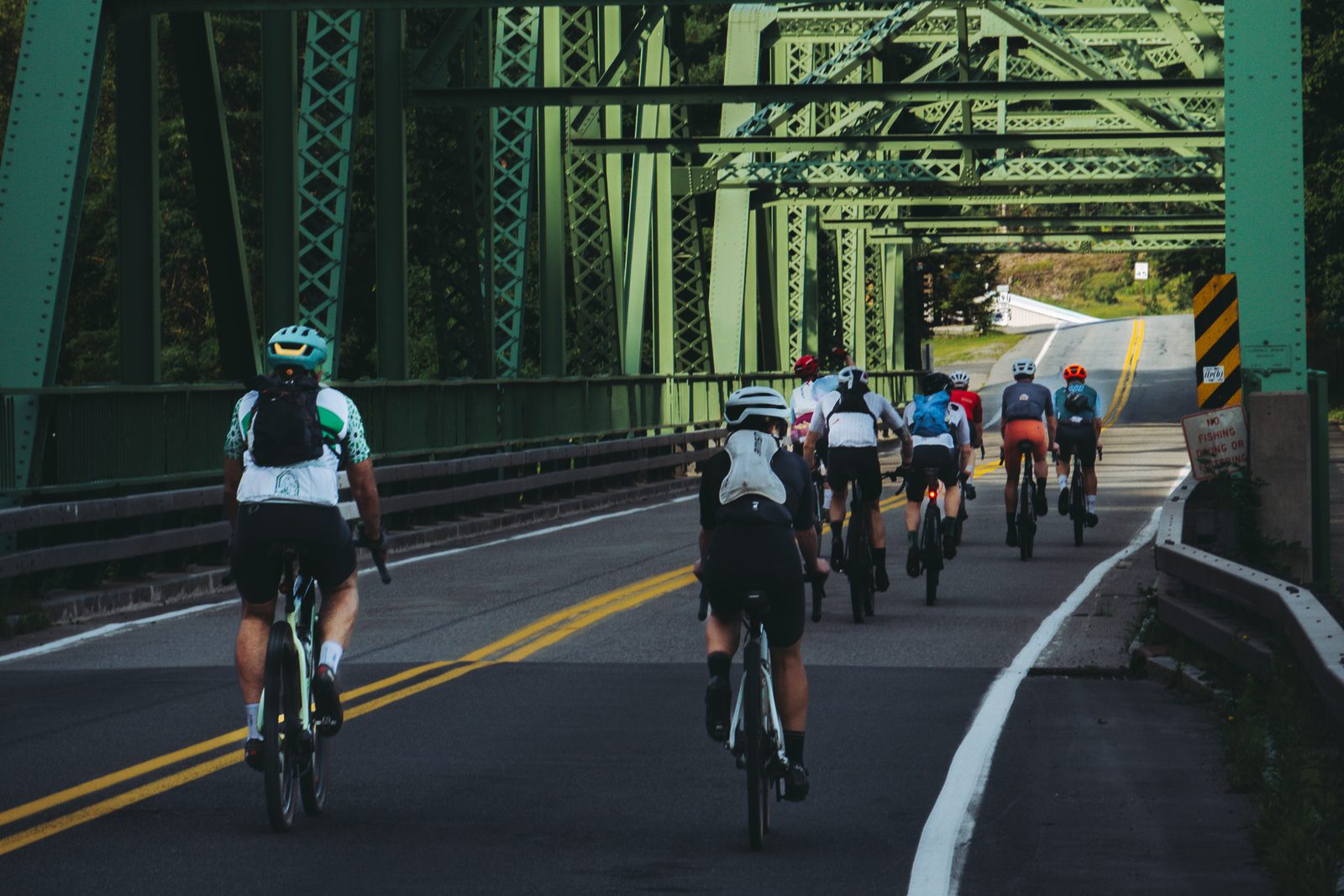 The whole field rolling out together across a green steel truss bridge in the morning.
