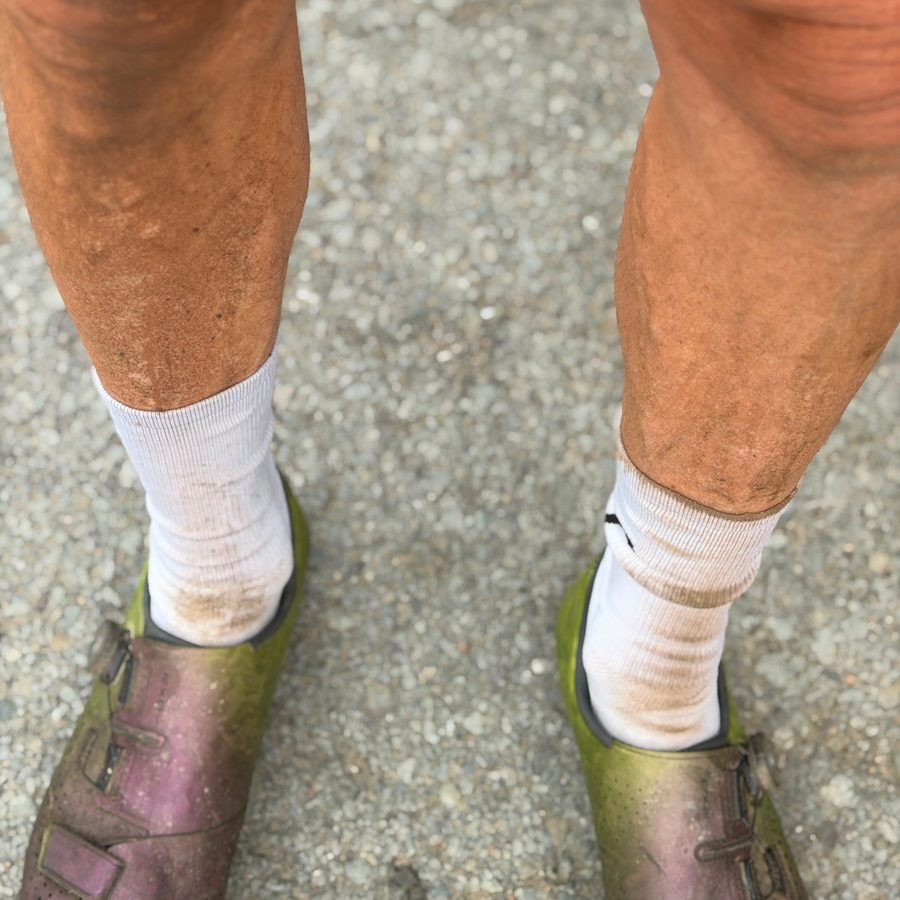 Close up of a rider's calves and shoes, caked in a tan line of gravel dust.